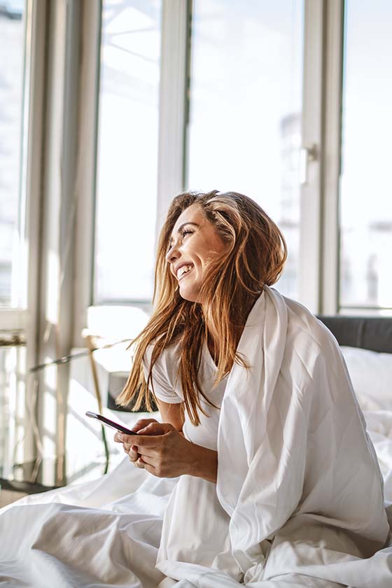 Woman on her bed laughing with someone on her phone